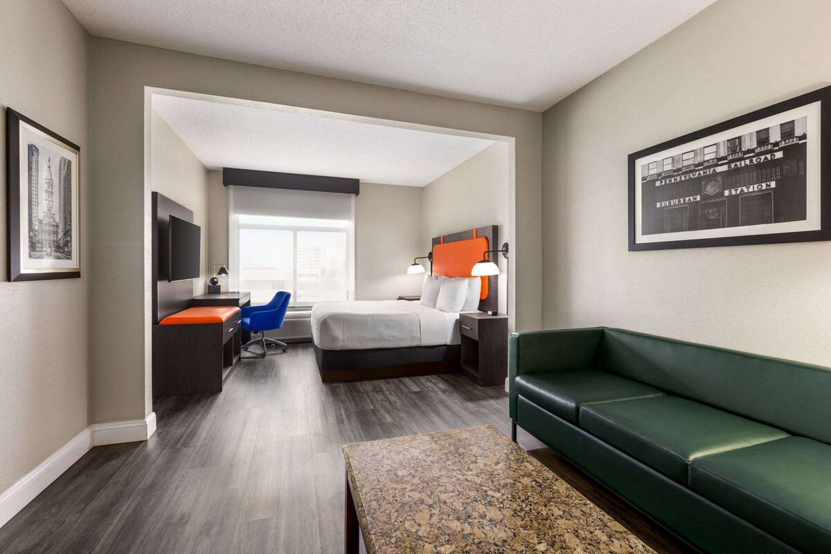 Une chambre d’hôtel moderne avec un lit, un bureau, un canapé vert et une grande fenêtre.