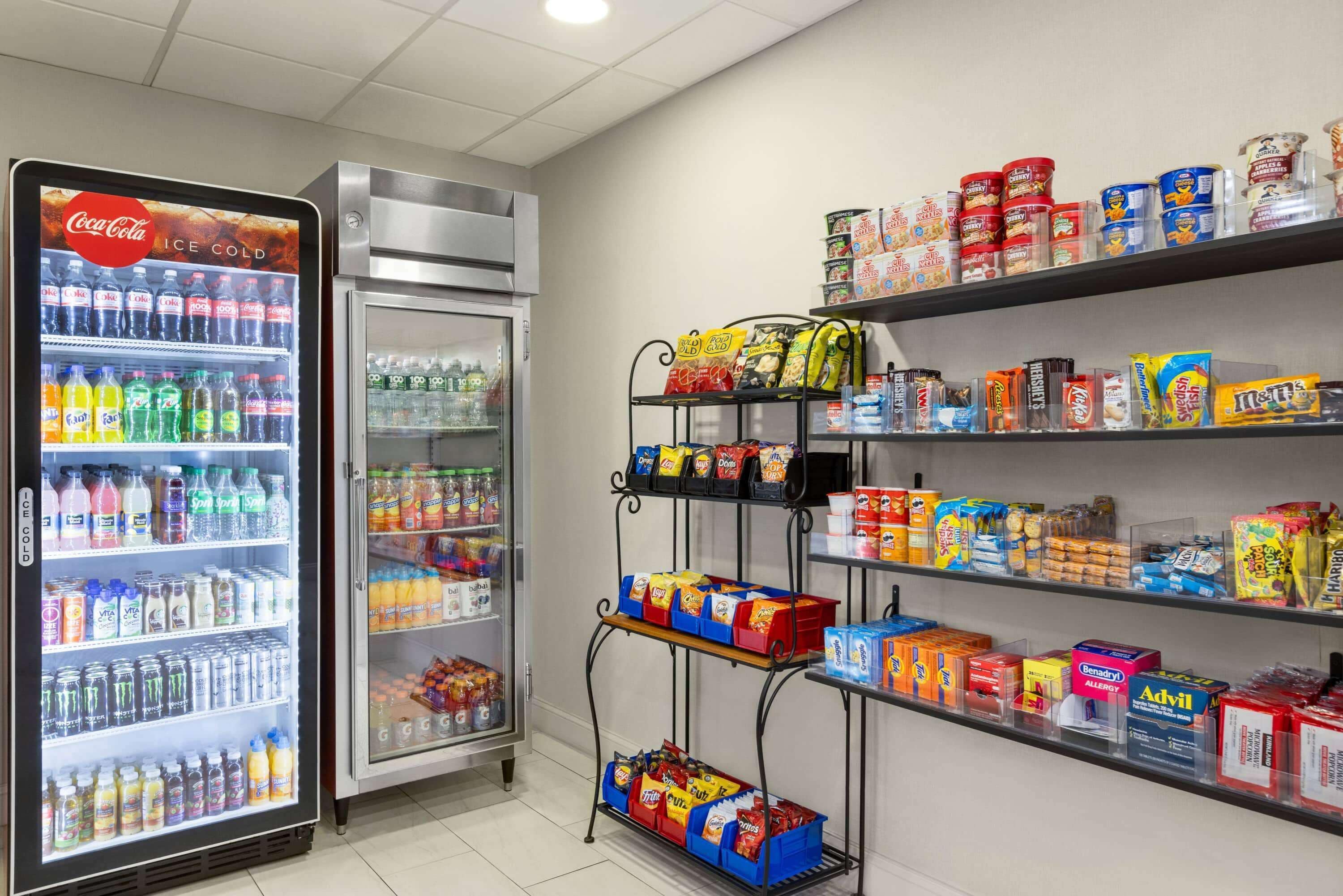 A vending area with a Coca-Cola refrigerator, a freezer, and shelves stocked with snacks and drinks.