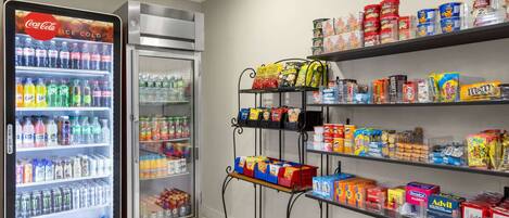 A vending area with a Coca-Cola refrigerator, a freezer, and shelves stocked with snacks and drinks.
