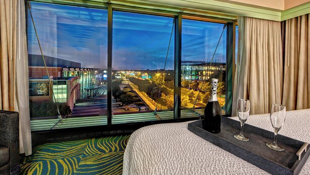 A hotel room with a large window, a bed, a bedside table with two glasses, and a patterned carpet. - SpringHill Suites Marriott Norfolk Old Dominion University (Norfolk)