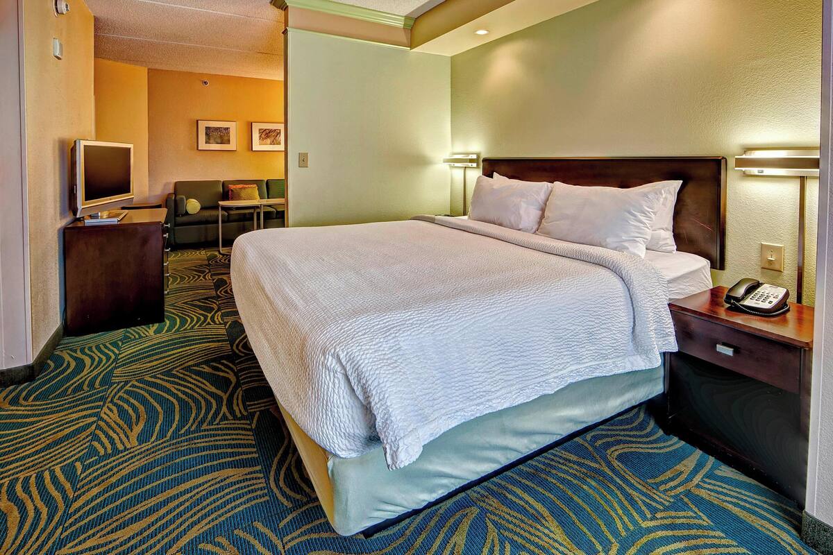 A hotel room with a large bed, a desk with a computer, a TV, and a seating area with a couch and chairs.