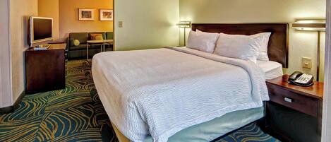 A hotel room with a large bed, a desk with a computer, a TV, and a seating area with a couch and chairs.