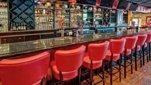 A bar area with red bar stools, a variety of bottles and glasses on shelves, and a counter with a cash register. - SpringHill Suites Marriott Norfolk Old Dominion University (Norfolk)