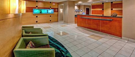 A hotel lobby with a reception desk, seating area, and a large flat-screen TV.