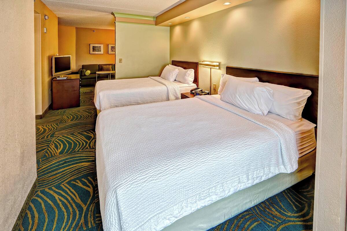 A hotel room with two beds, a television, a desk, and a lamp.
