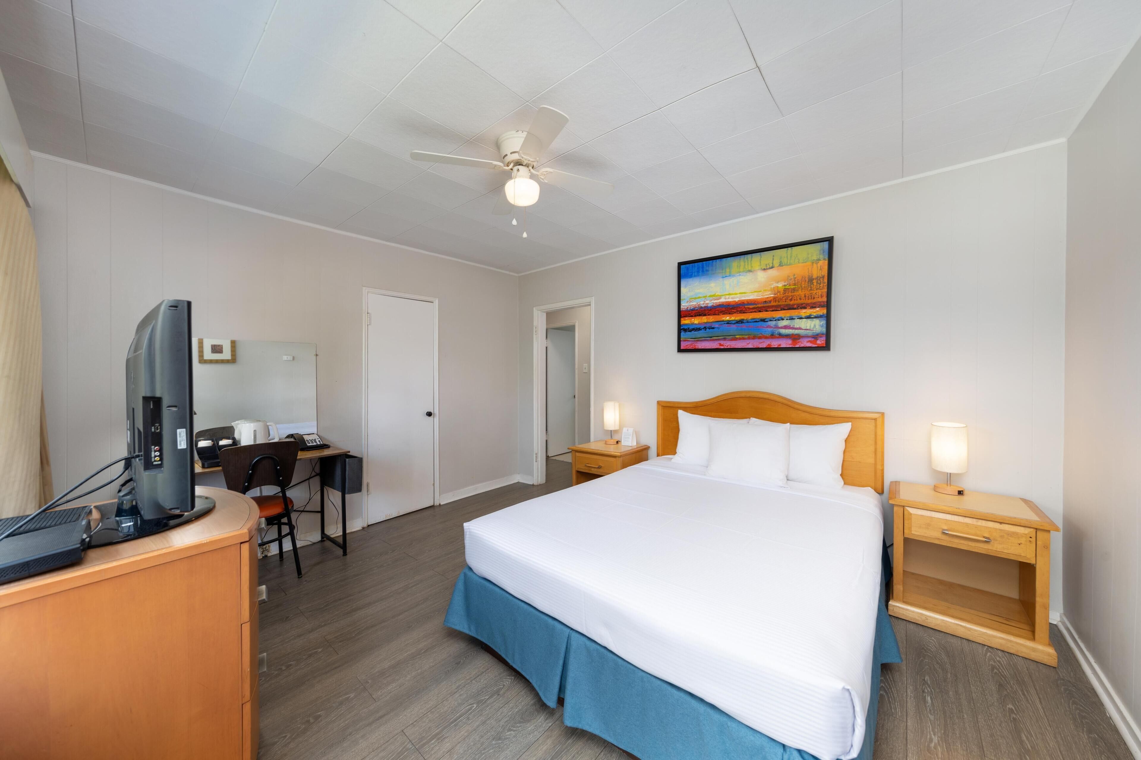 Una habitación de hotel con cama, escritorio, computadora y ventilador de techo.