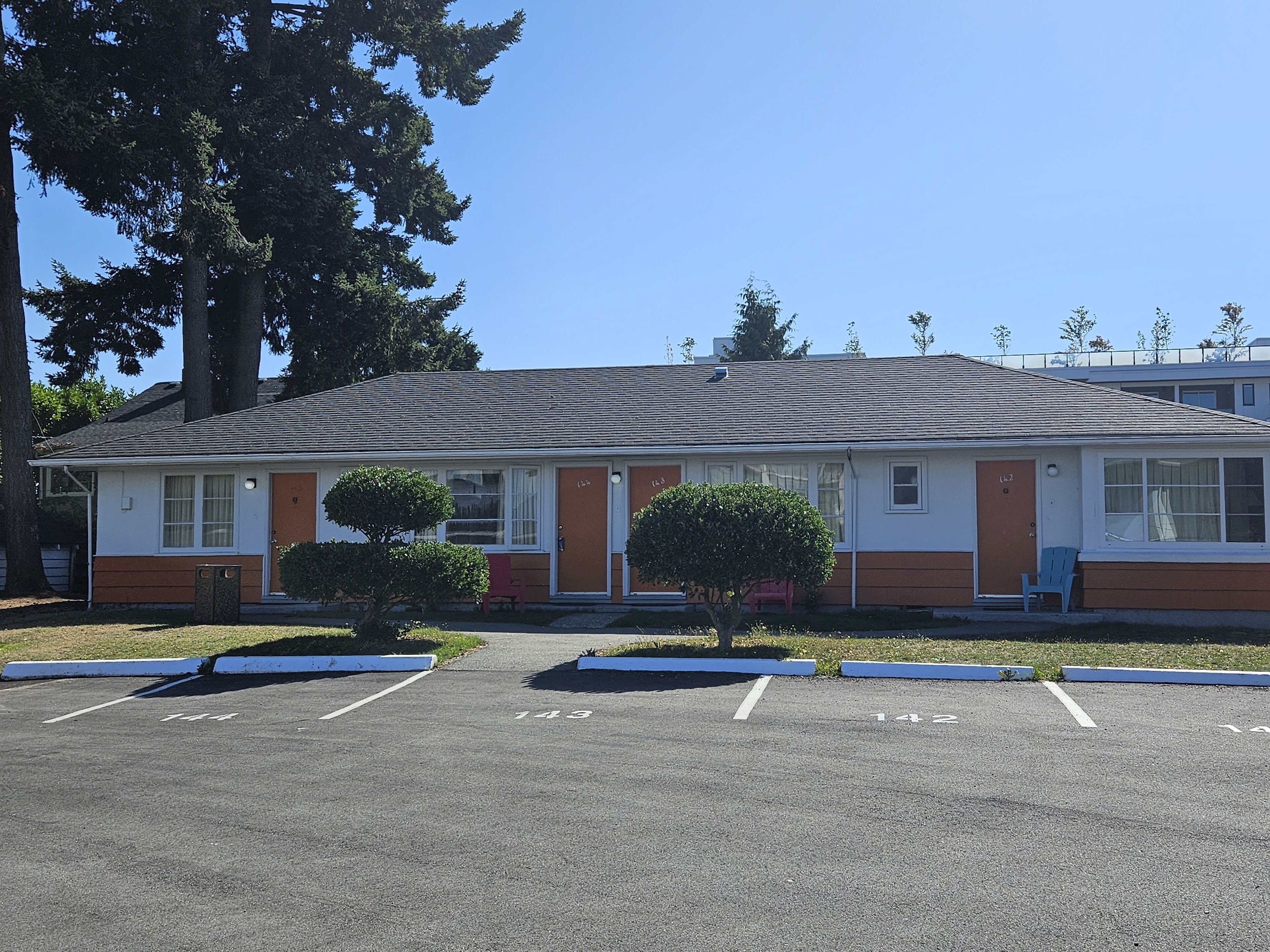 A motel with a single-story structure, a parking lot with marked spaces, and a small front yard with a trimmed bush.