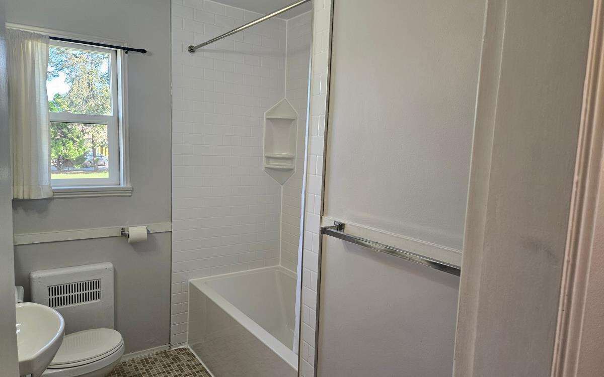 Een badkamer met toilet, douche en raam.