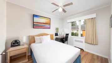 Una habitación de hotel con cama, escritorio, silla y ventilador de techo.