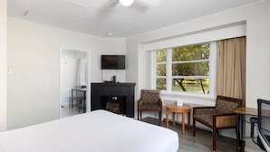 A hotel room with a large bed, a fireplace, a TV, a desk, and a window with a view of trees. - 2400 Motel (Vancouver)