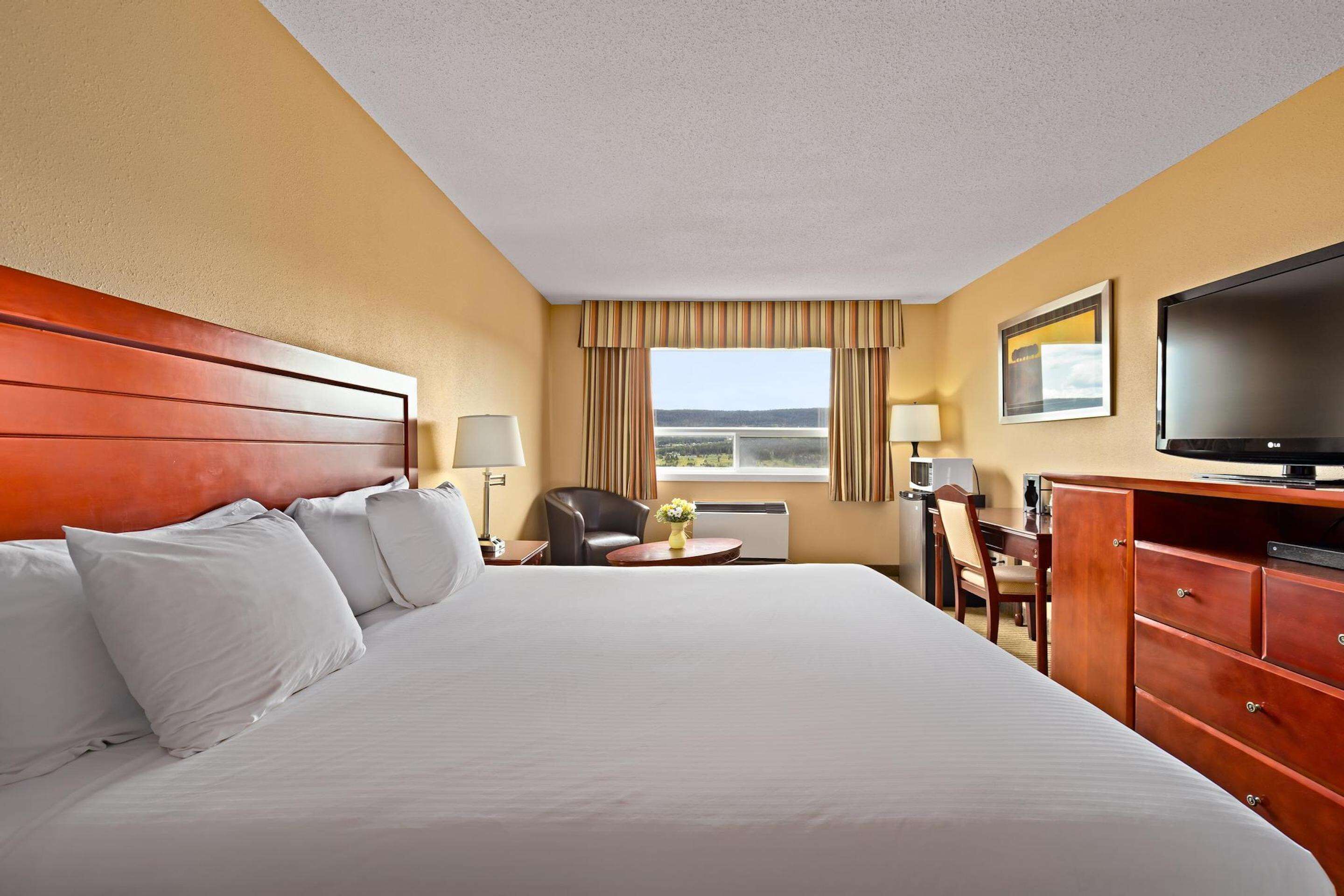 A hotel room with a large bed, a desk, a chair, a television, and a window with curtains.