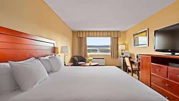 A hotel room with a large bed, a desk, a chair, a television, and a window with curtains.