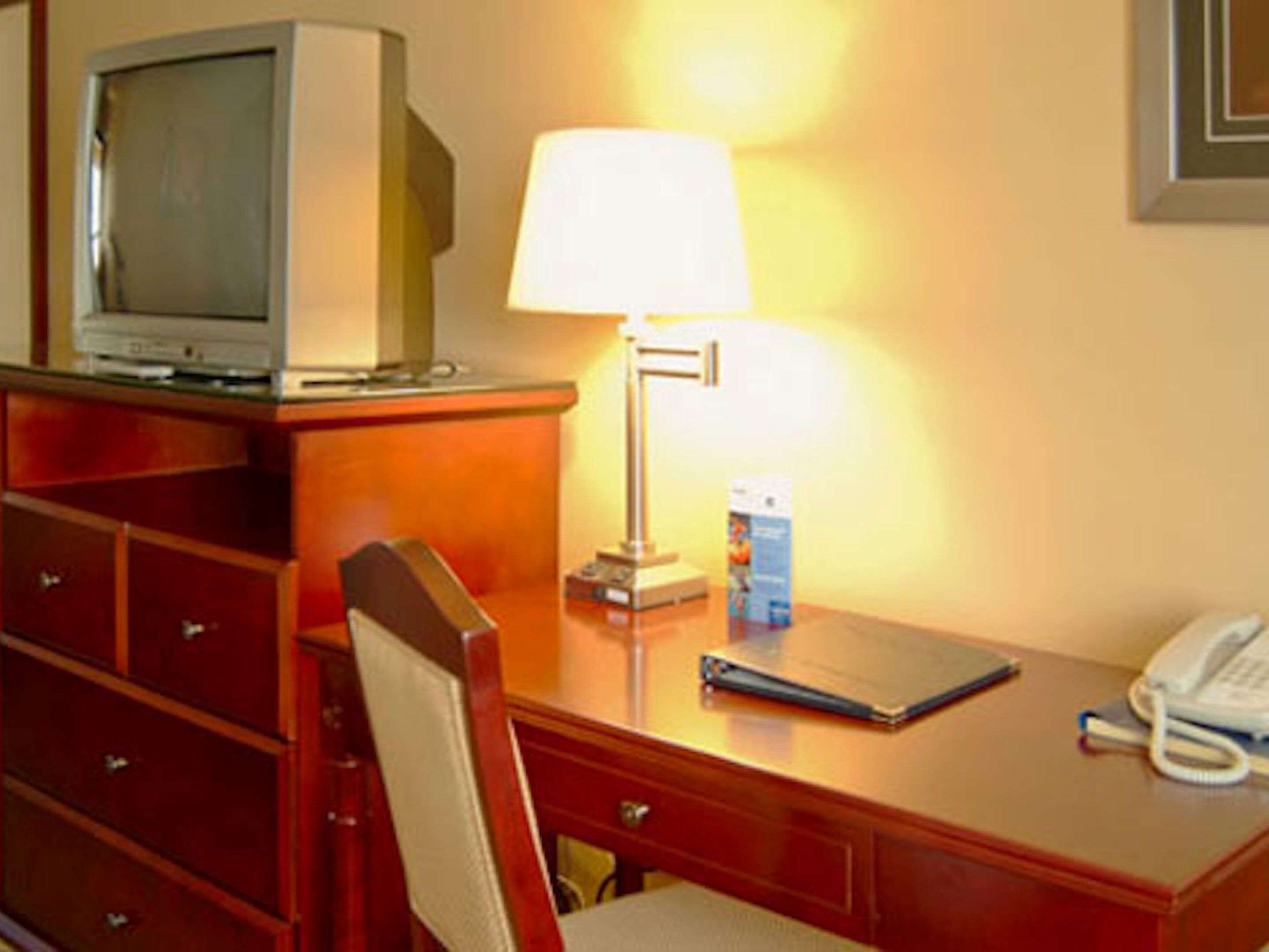 A hotel room with a wooden desk, a television, a lamp, a telephone, and a chair.