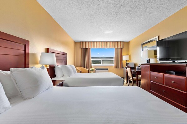 A hotel room with two beds, a TV, a desk, and a window with curtains. - Coast Fraser Inn (Williams Lake)