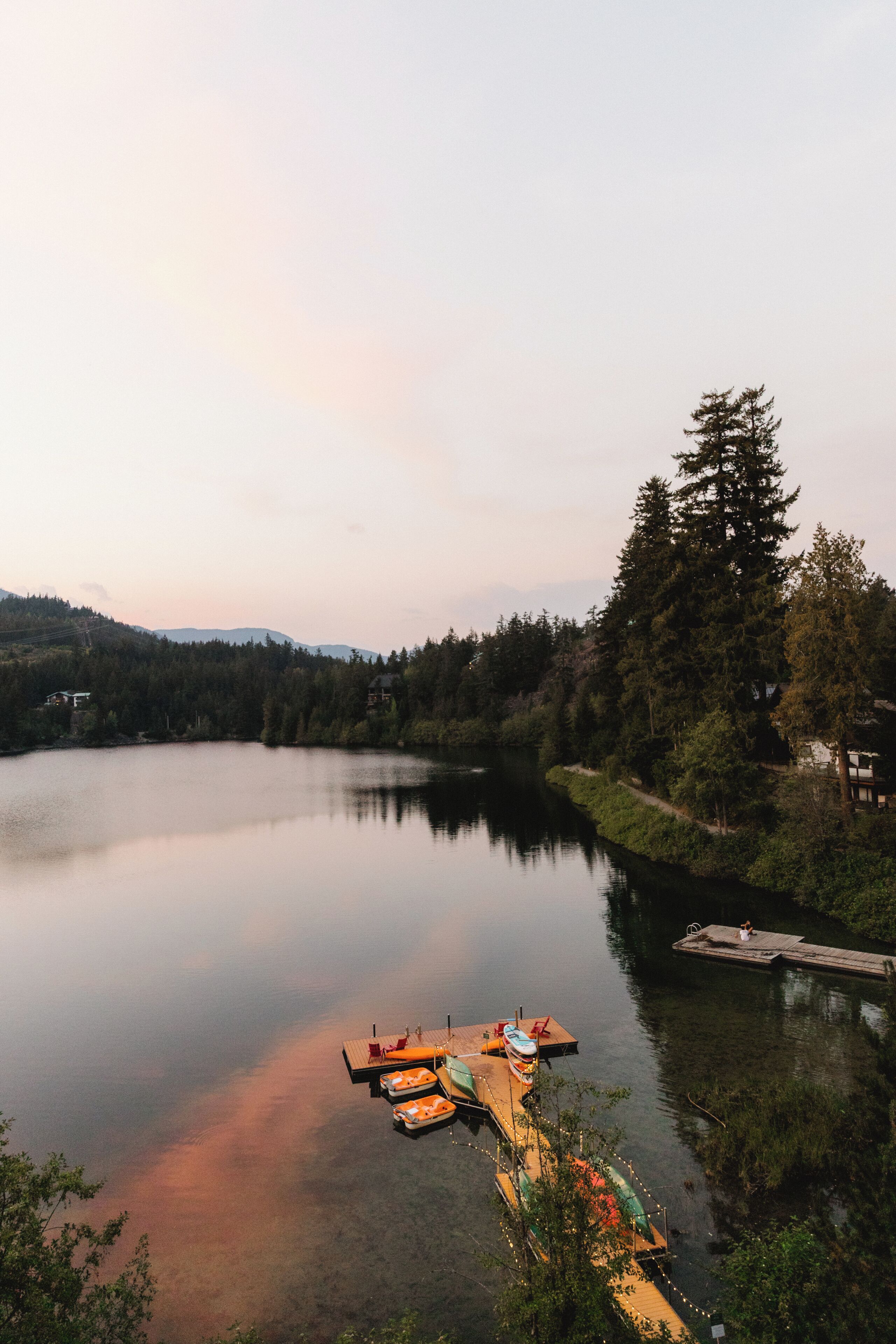 A calm lake with a dock and boats, surrounded by trees and hills.
