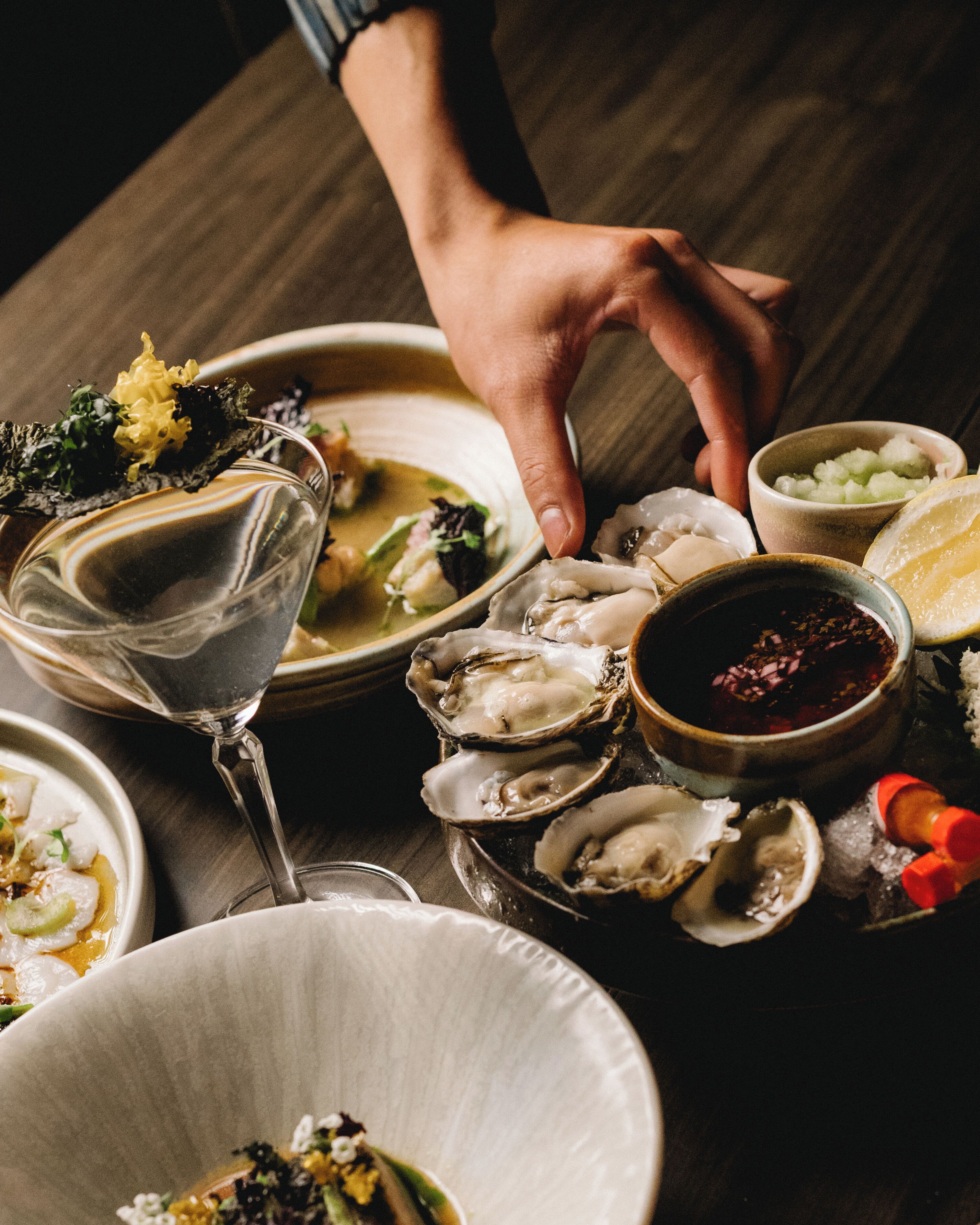 Une table à manger dressée avec différents plats, notamment des huîtres, un verre de vin et un bol de soupe.