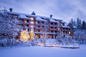 A multi-story lodge with a snow-covered exterior and warm lighting. - Nita Lake Lodge (Whistler)