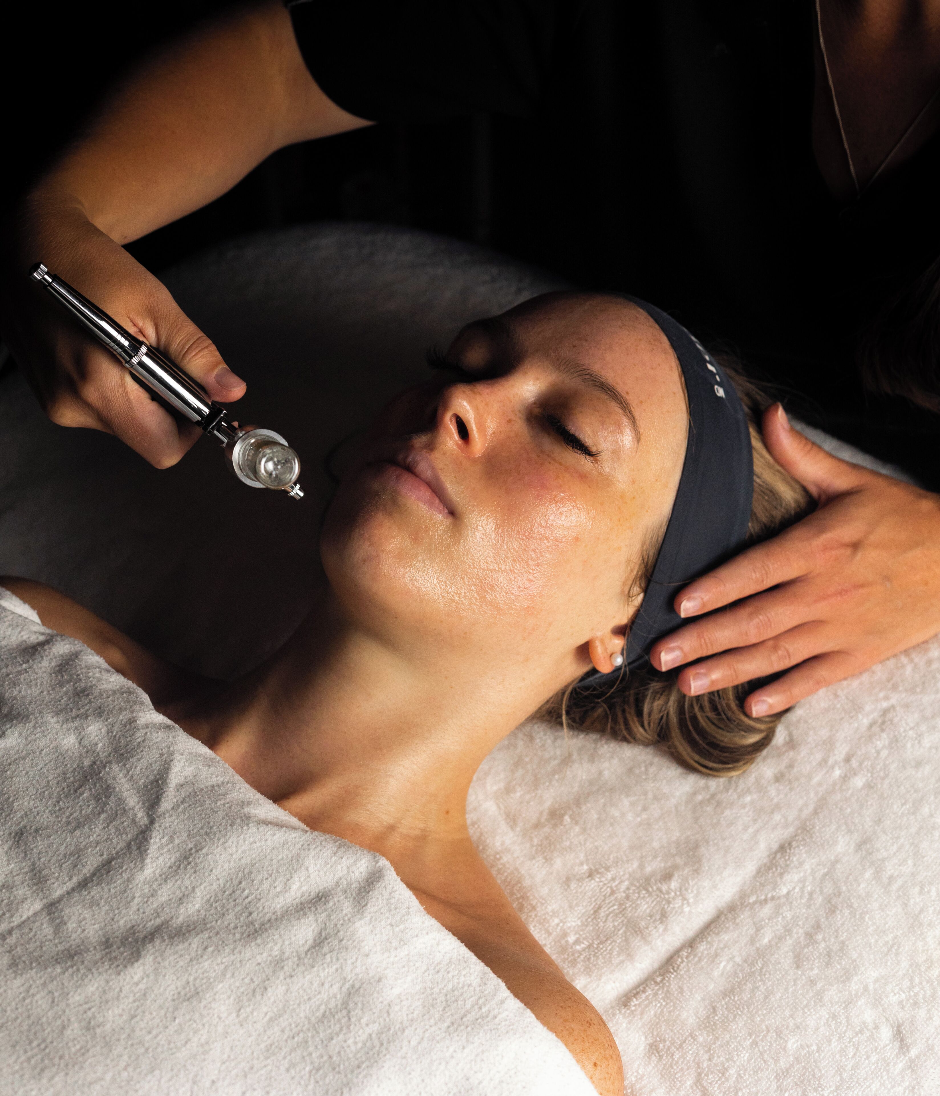 A person lying down with a device being used on their head, possibly for a medical or beauty treatment.