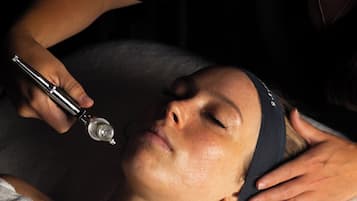 A person lying down with a device being used on their head, possibly for a medical or beauty treatment.