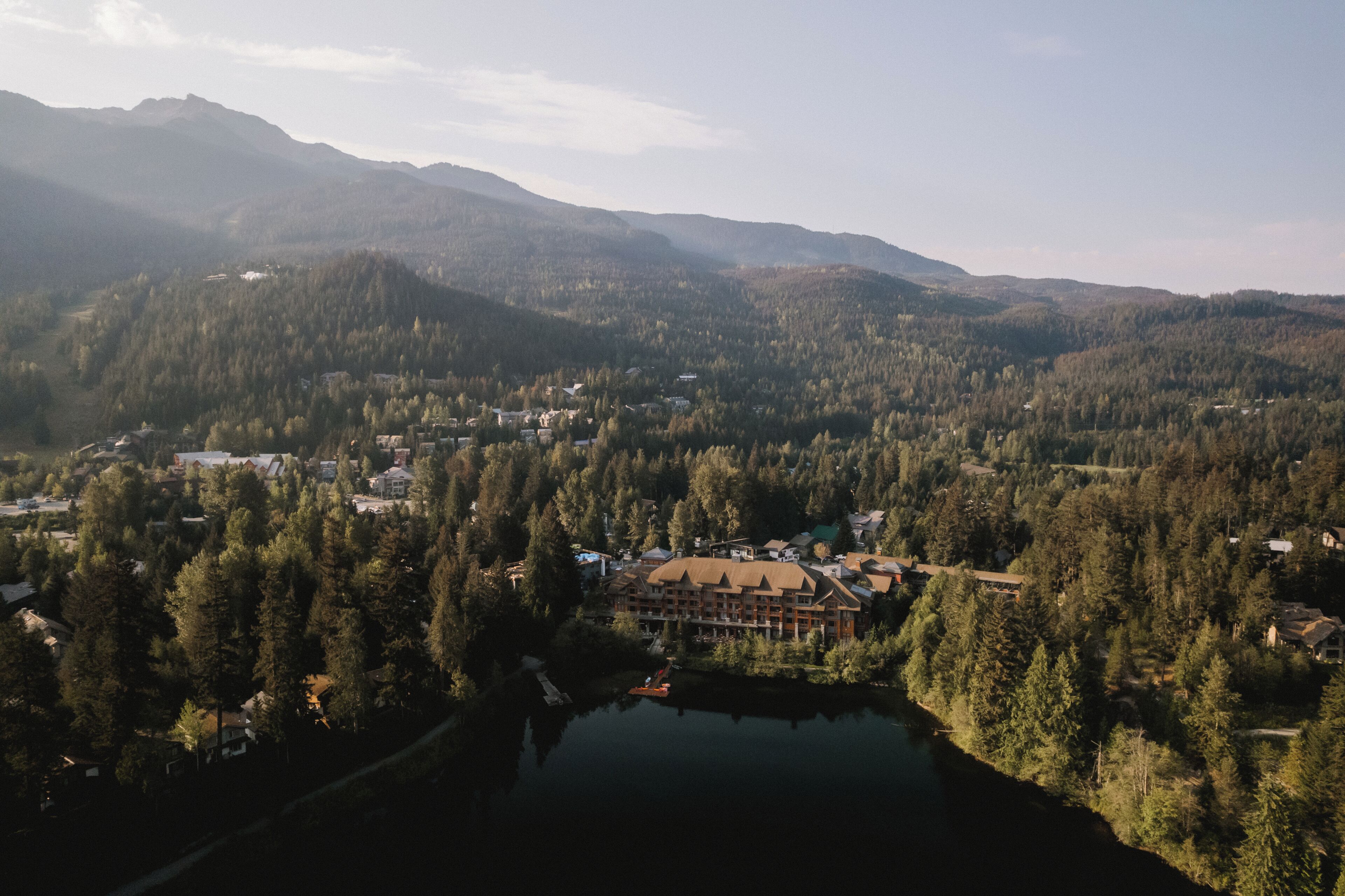 Een lodge omgeven door dicht bos en bergen, met een meer op de voorgrond.