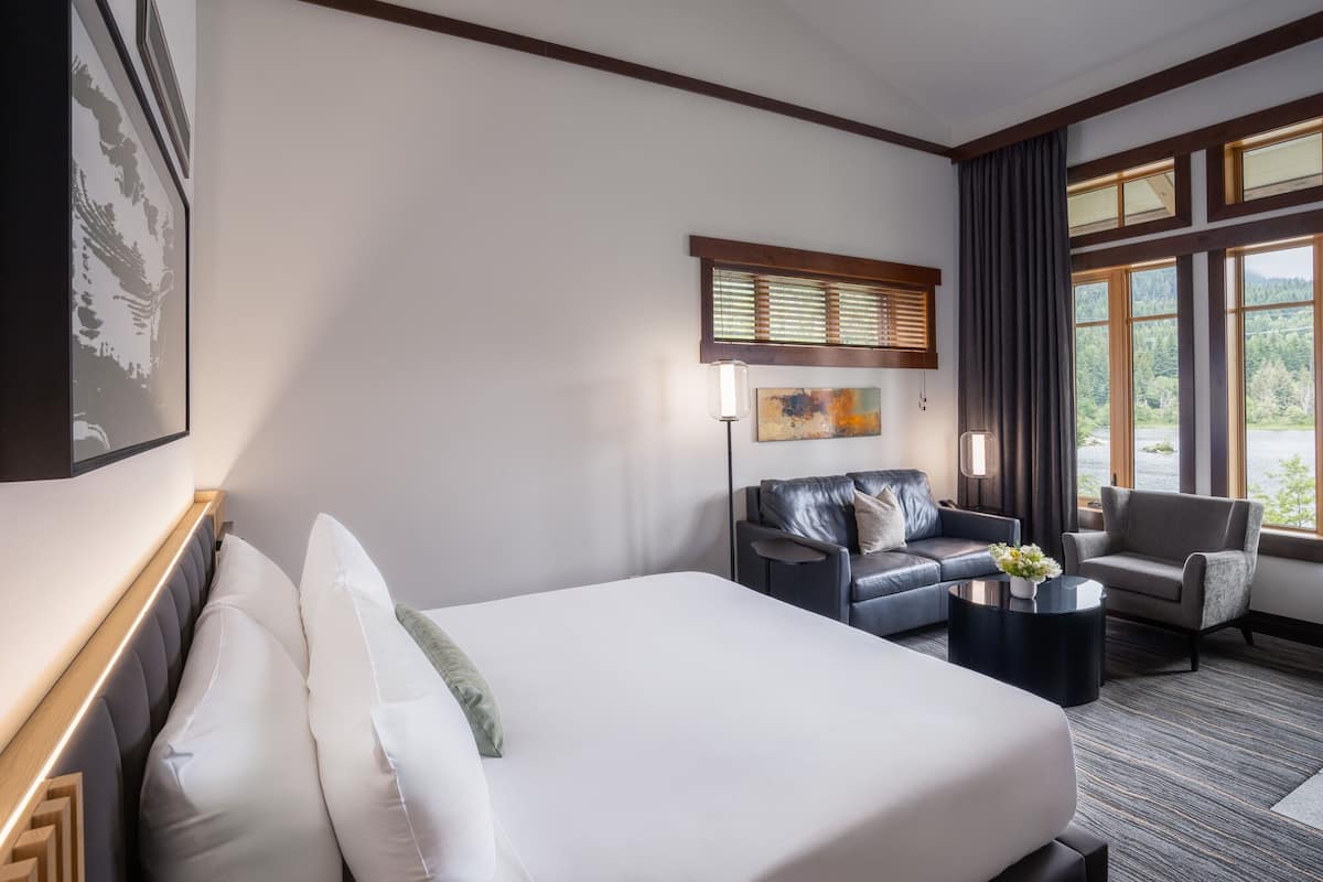 Een hotelkamer met een groot bed, een sofa, een fauteuil, een salontafel en een schilderij aan de muur.