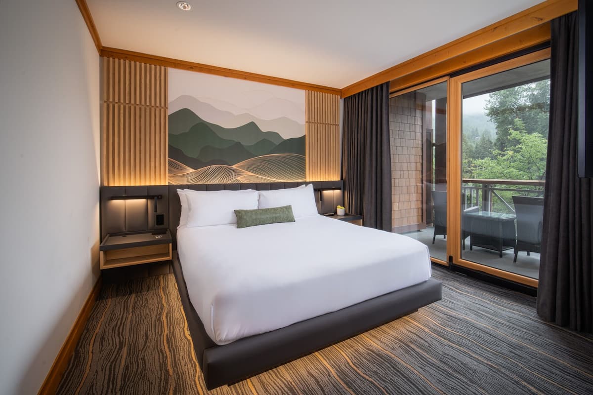 Een hotelkamer met een groot bed, uitzicht op de natuur en een schilderij aan de muur.