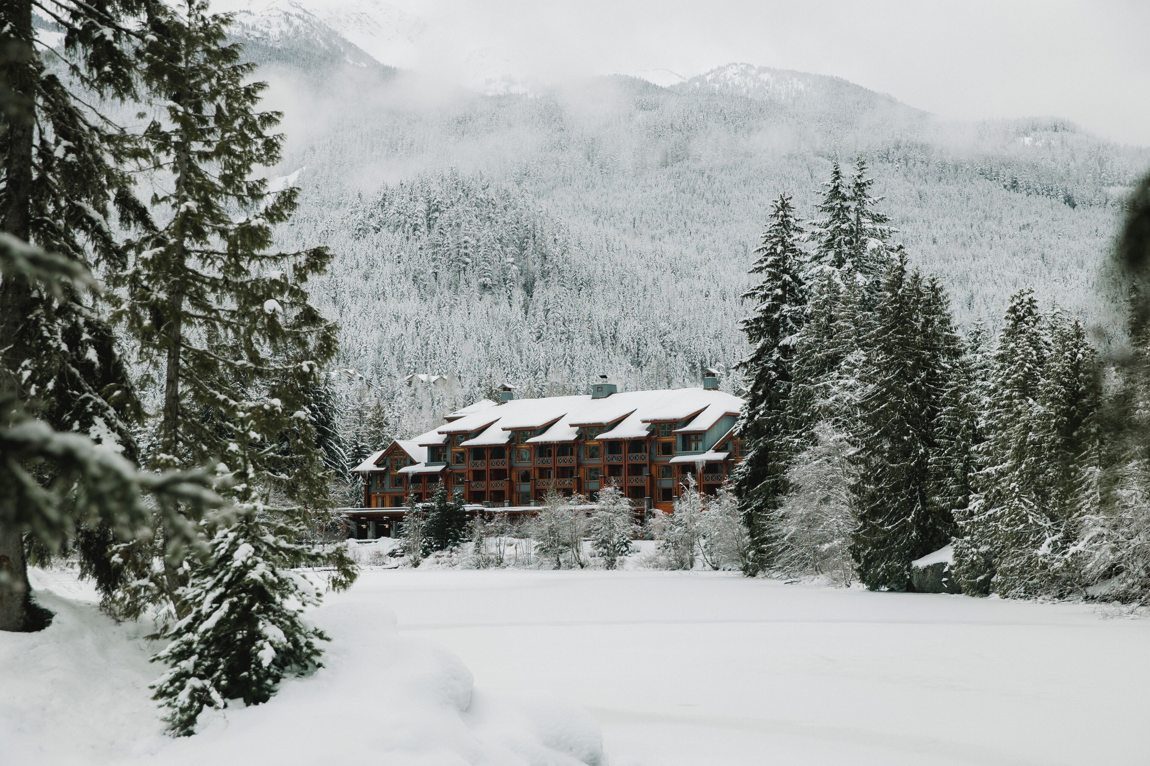 A lodge with a symmetrical facade, surrounded by snow-covered trees and a mountainous backdrop.