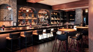 A bar area with multiple seating options, a stone wall, and a variety of bottles on shelves.