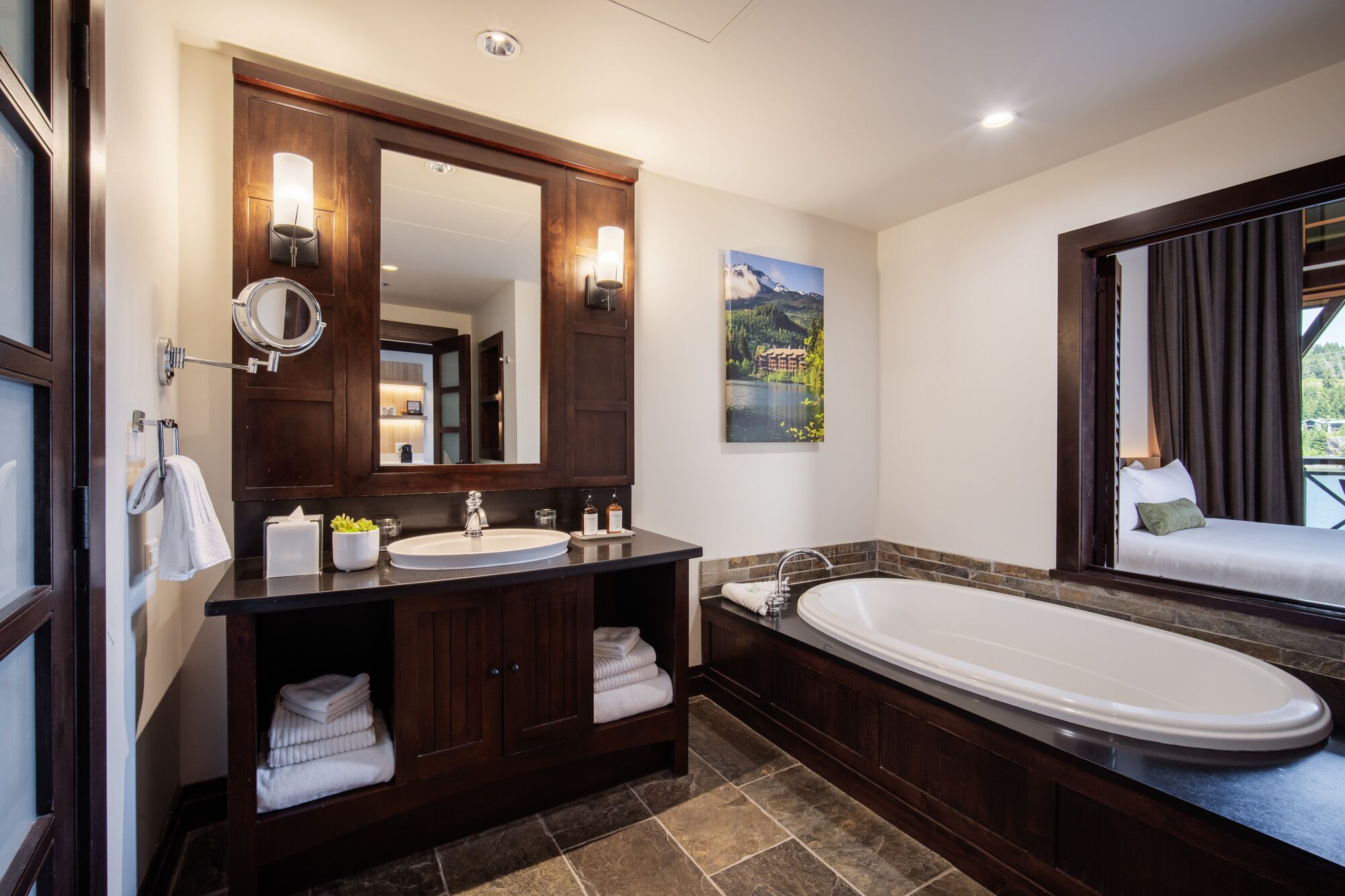 A modern bathroom with a large mirror, two sinks, a bathtub, and a window with curtains.