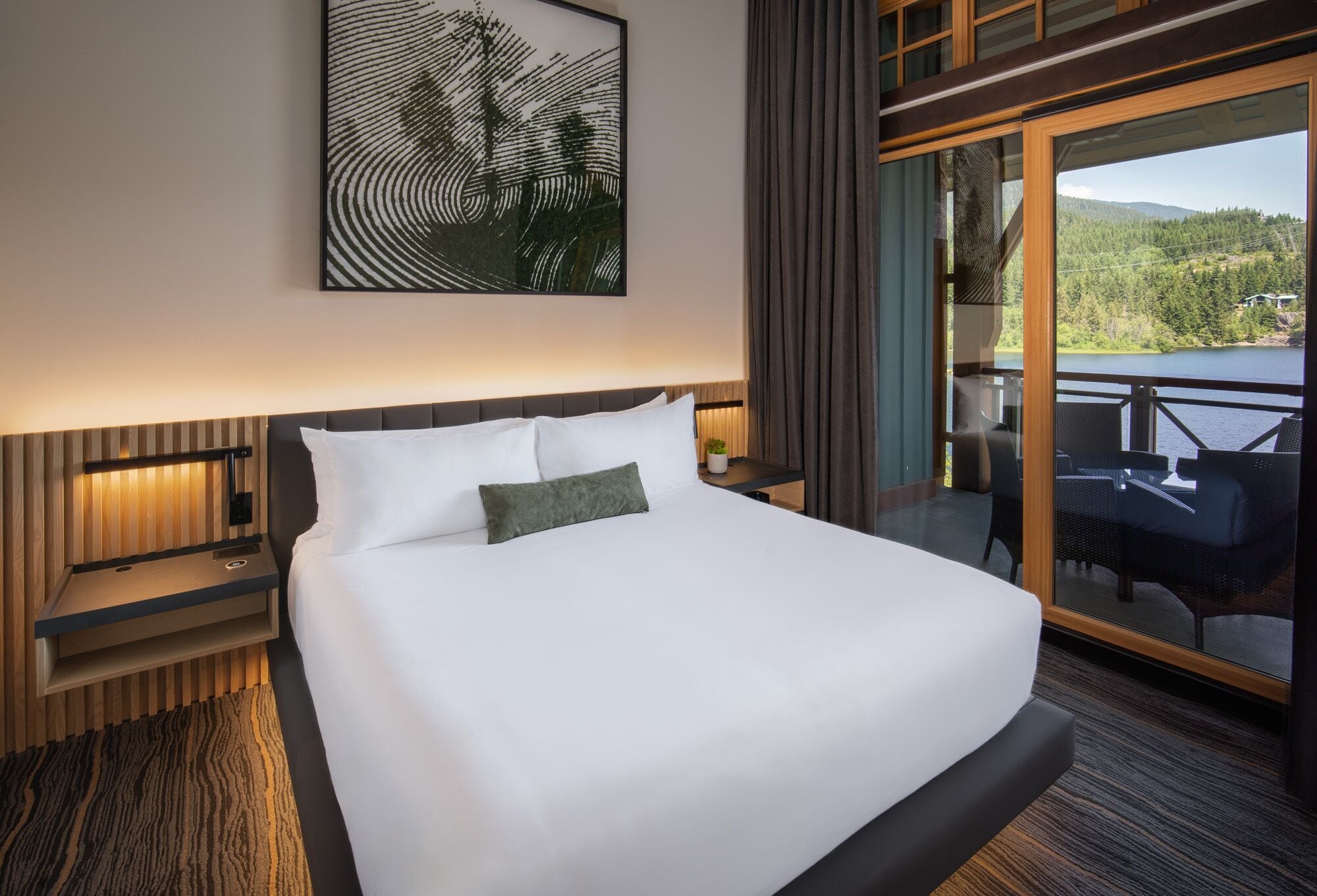 Una camera d'albergo con un letto grande, vista su un lago e un balcone con mobili da esterno.