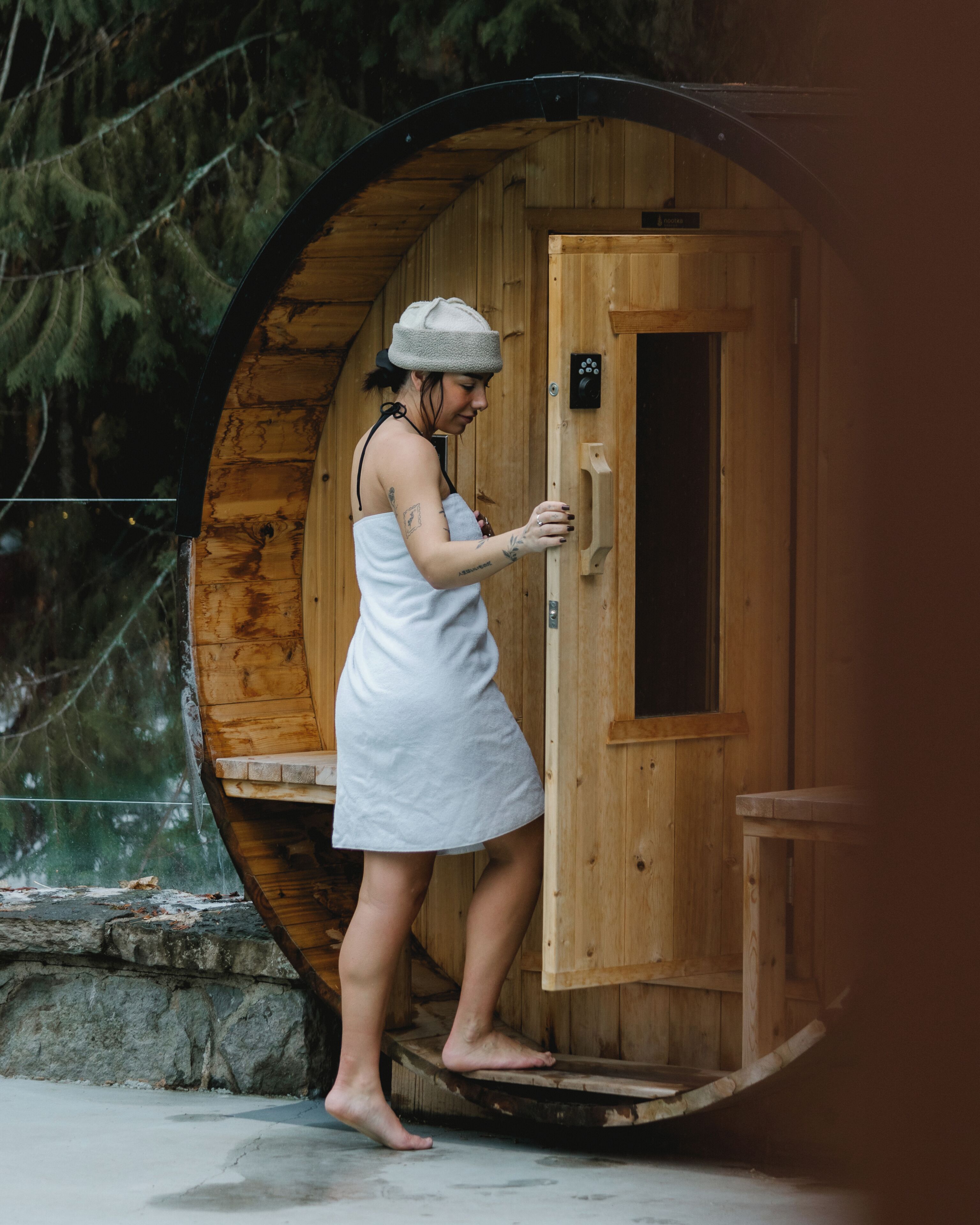 A person in a white dress standing at the entrance of a wooden, circular structure with a door and a small window.