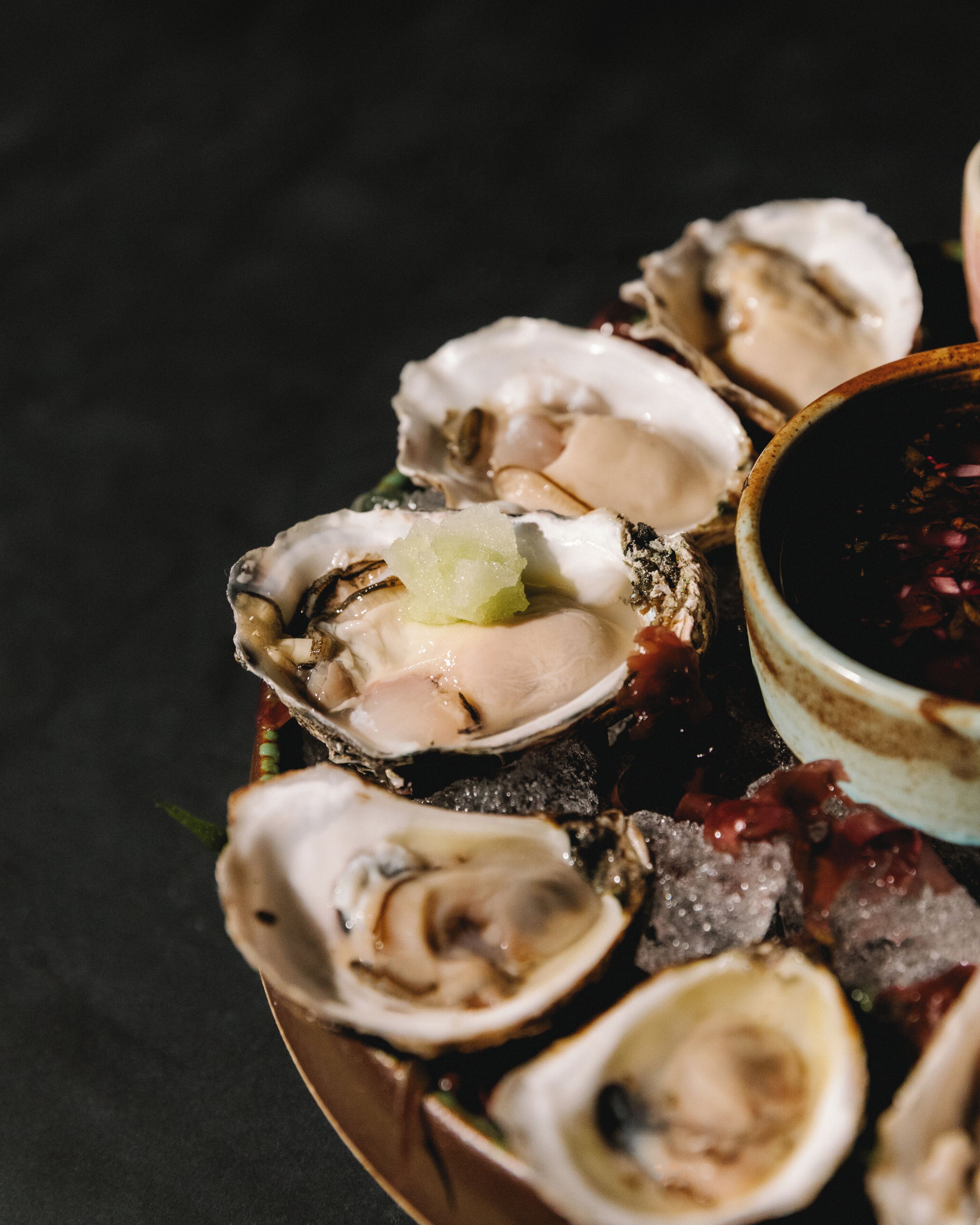 Un plato de ostras con un recipiente pequeño de salsa.