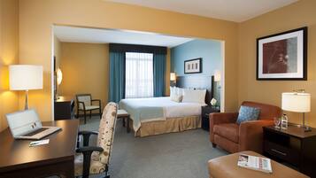 A hotel room with a bed, a desk with a laptop, a chair, a sofa, and a nightstand with a lamp.