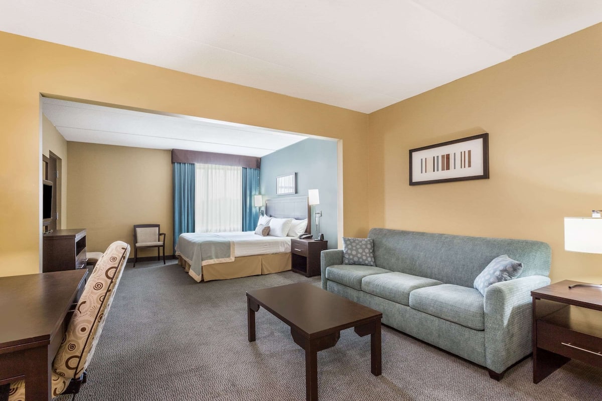 A hotel room with a bed, a sofa, a coffee table, a desk, and a TV.
