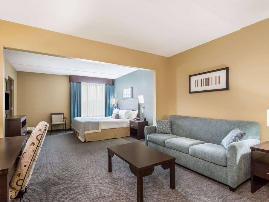 Una habitación de hotel con cama, sofá, mesa de centro, escritorio y televisión.