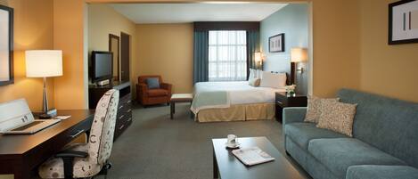 A hotel room with a desk, chair, bed, and sofa.