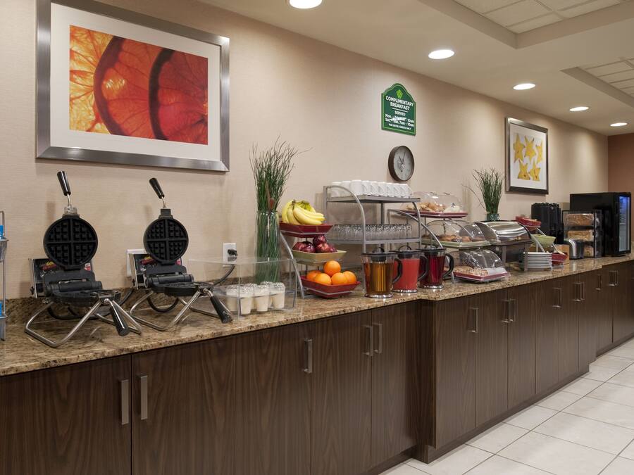 A breakfast bar with waffle makers, fruit, and beverages.