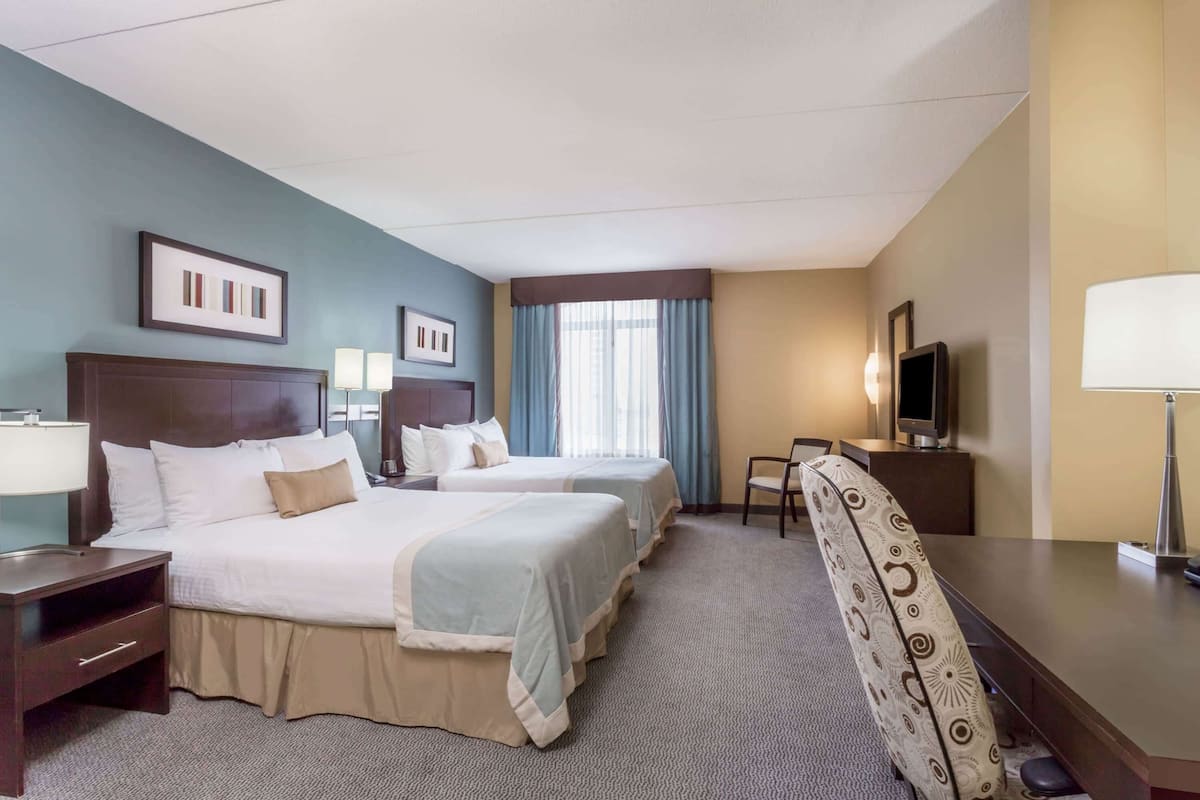 A hotel room with two beds, a desk, a chair, a TV, and a window with curtains.