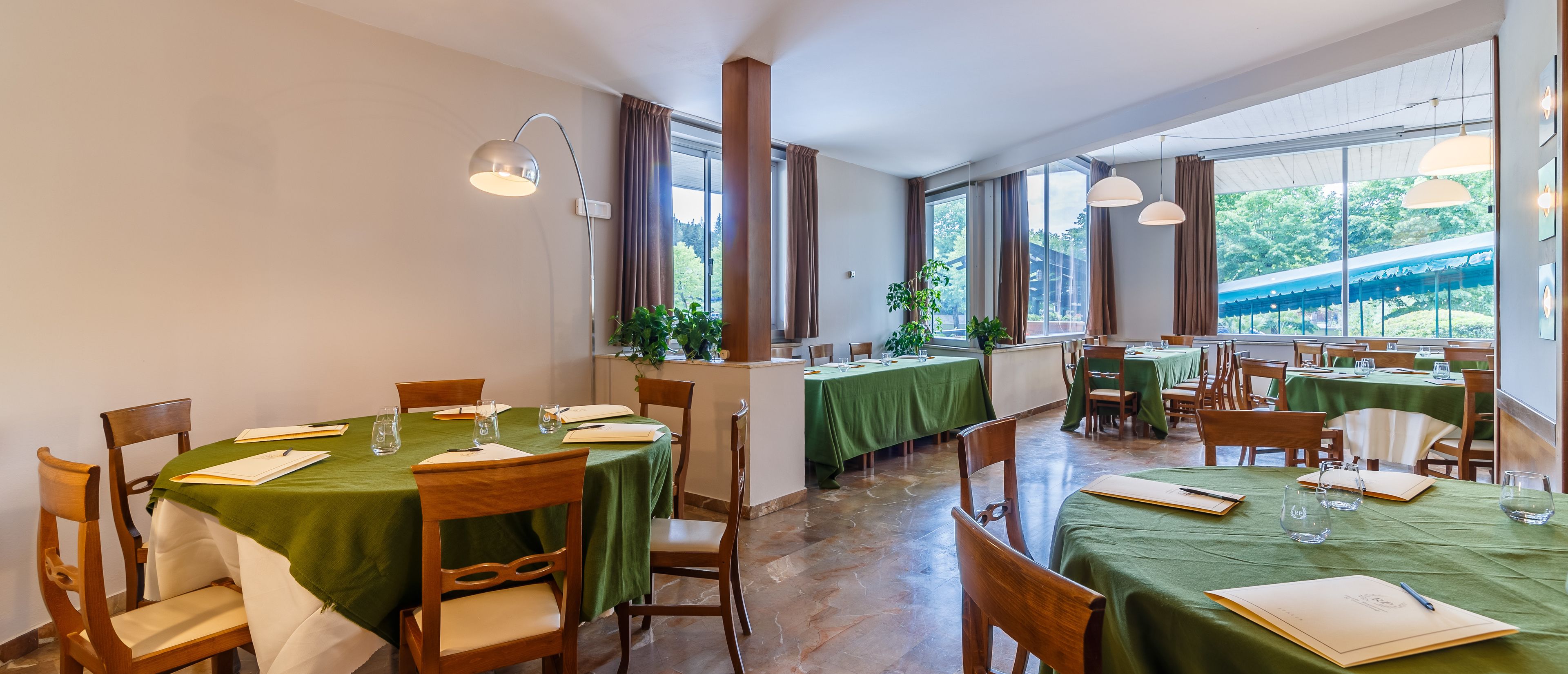 Un espace repas avec des tables dressées pour quatre personnes, des chaises en bois et des nappes vertes.