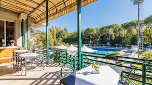 An outdoor patio with tables and chairs, a pool area, and a view of trees and hills. - Hotel Country Club (Capannori)