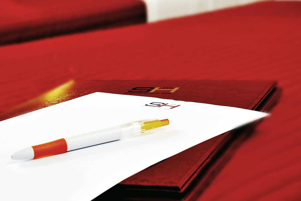 A hotel room with a bed, a red pillow, and a pen on a piece of paper.
