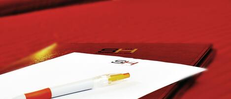 A hotel room with a bed, a red pillow, and a pen on a piece of paper.