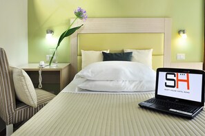 A hotel room with a bed, a laptop on the bed, a nightstand with a lamp, and a chair.