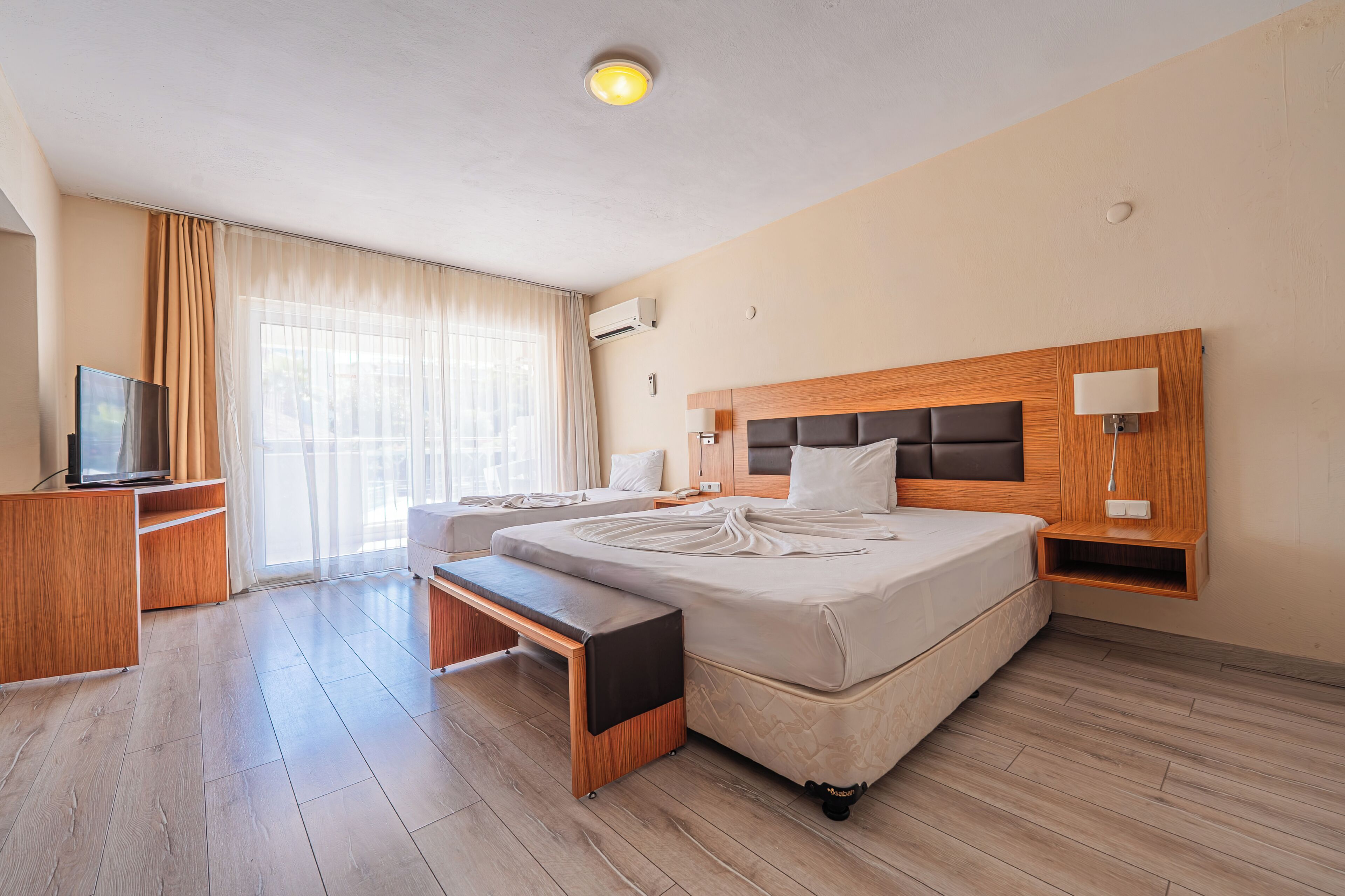 A hotel room with a large bed, a bedside table, a TV, and a window with curtains.