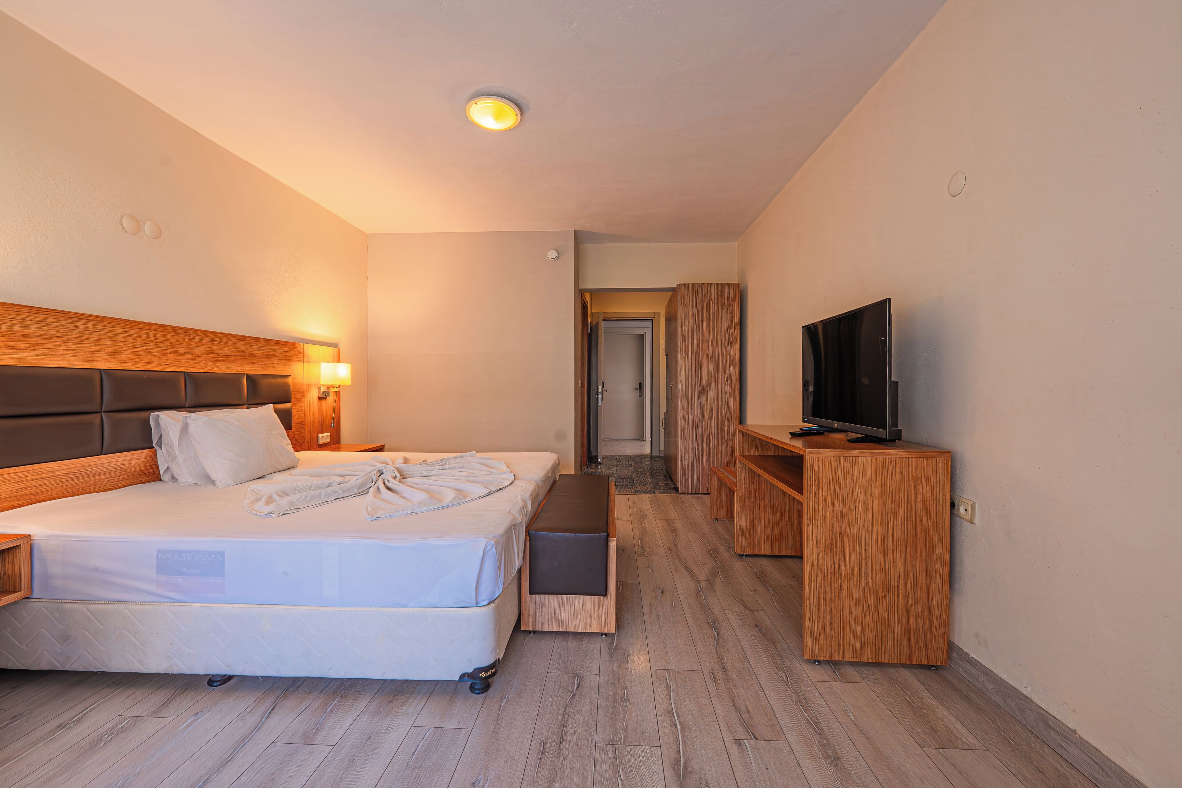 A hotel room with a bed, a television, a wooden cabinet, and a bathroom door.