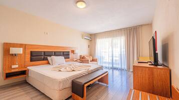 Quarto de hotel com cama, mesa de cabeceira, luminária, ar condicionado e televisão sobre um móvel de madeira.