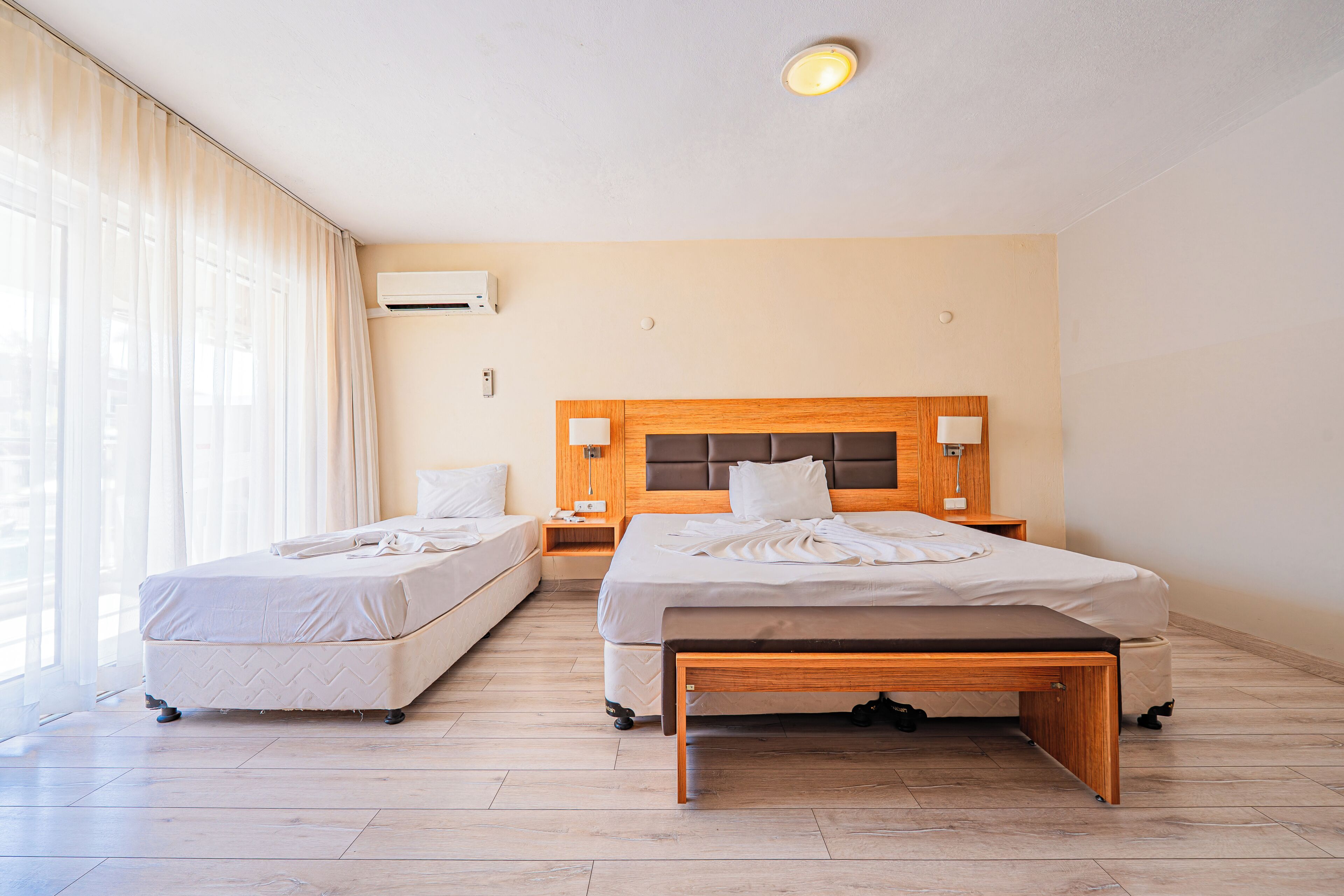 Een hotelkamer met twee bedden, een houten hoofdbord, een nachtkastje met een lamp en een airconditioning op de muur.