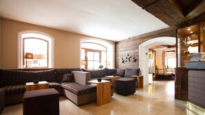 A spacious lobby with a checkered sofa set, wooden tables, and a tiled floor. - Rennrad- & Triathlonhotel Jakob (Fuschl am See)