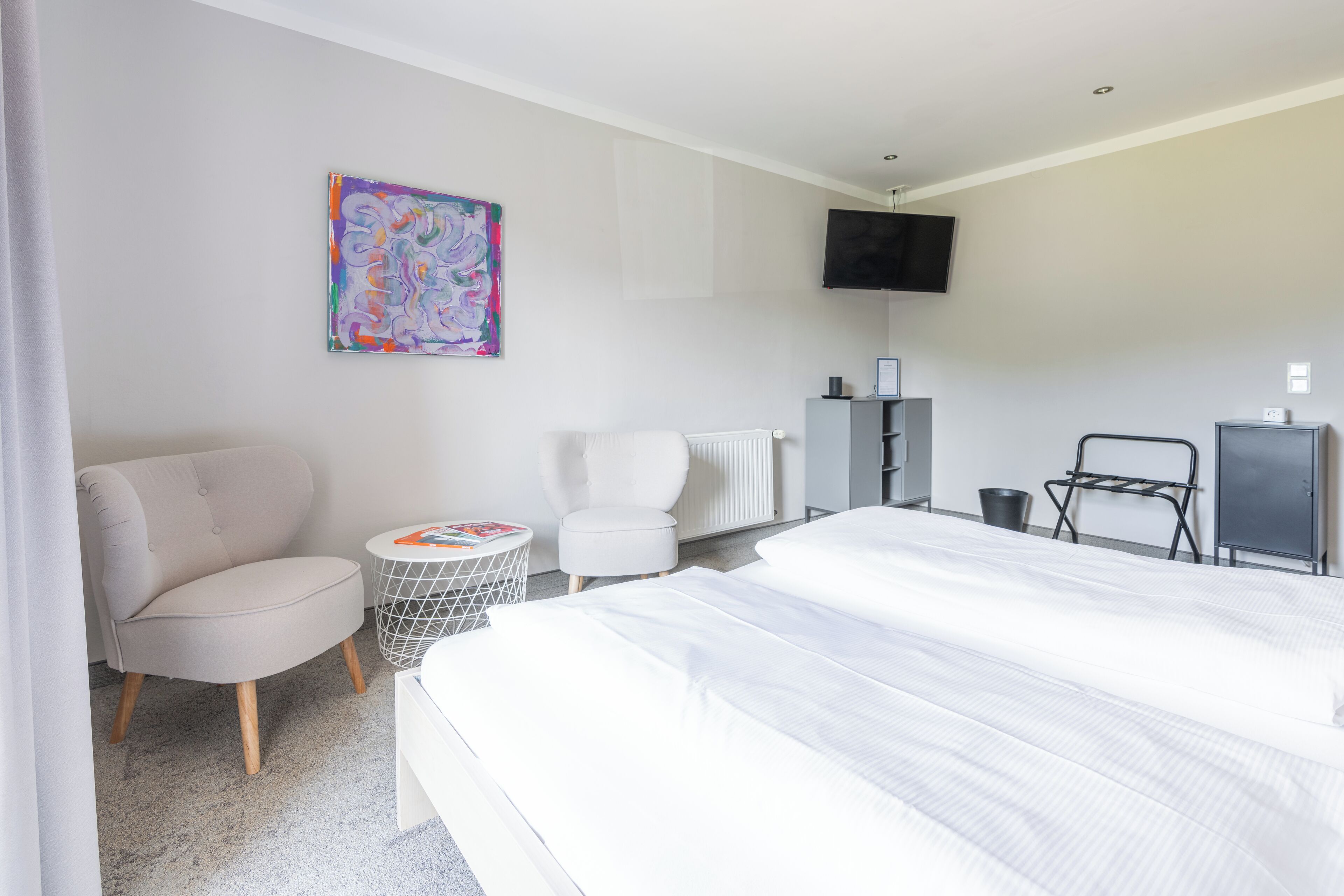 Una habitación de hotel moderna con una cama grande, una silla, una mesita redonda, un televisor y un radiador.