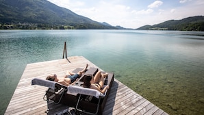 A wooden pier with lounge chairs and a towel, overlooking a calm lake with mountains in the background. - Rennrad- & Triathlonhotel Jakob (Fuschl am See)